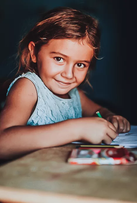 Criança sorri enquanto desenha e posa para a foto